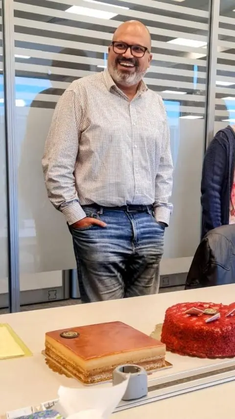 Peter GORGY laughing beside farewell cakes on a meeting-room table.