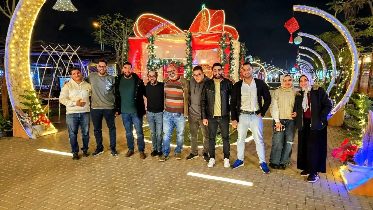 Peter GORGY with ten friends and colleagues at night, in front of a large illuminated gift-box decoration and arches of lights.