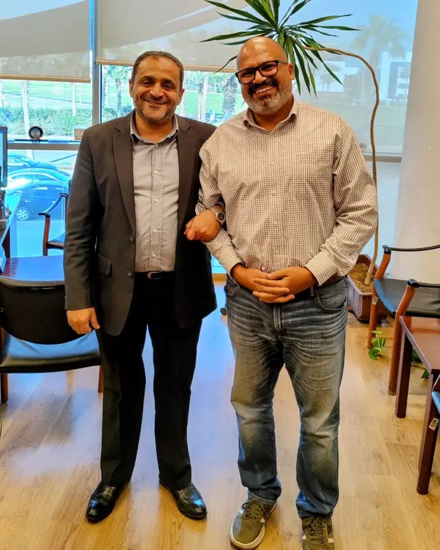 Peter GORGY smiling arm in arm with a colleague in an office.