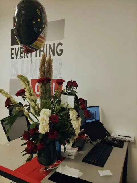 A desk with a large bouquet of red and white roses and a balloon.