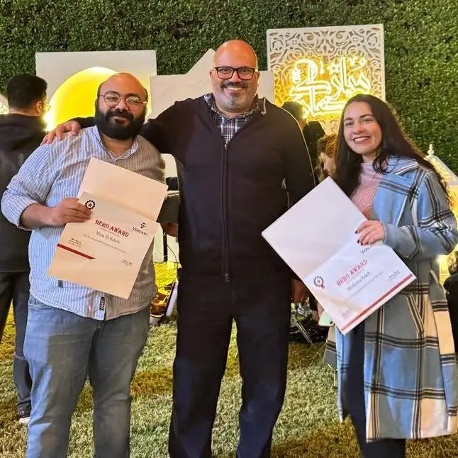 Peter GORGY standing between two colleagues holding Hero Award certificates at an outdoor evening event.