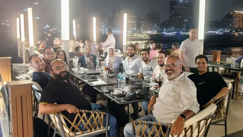 Peter GORGY with a group of colleagues around a table at a riverside restaurant at night.